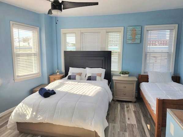 A bedroom with a bed, two nightstands, a ceiling fan, and a window with blinds.