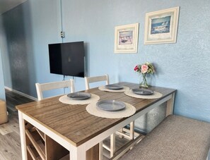 Une table à manger avec quatre chaises, un téléviseur à écran plat fixé au mur et deux tableaux encadrés accrochés au mur.