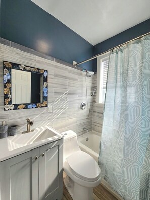 Une salle de bain avec des toilettes blanches, une douche dotée d’une porte en verre, un lavabo avec un plan-vasque en marbre et un miroir orné d’un cadre décoratif.
