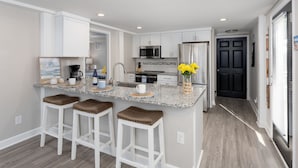 A modern kitchen with white cabinets, a granite countertop, and a central island with stools. - 2 Kitchens, 2 Living Rooms, Sleeps 10 (Surf City)
