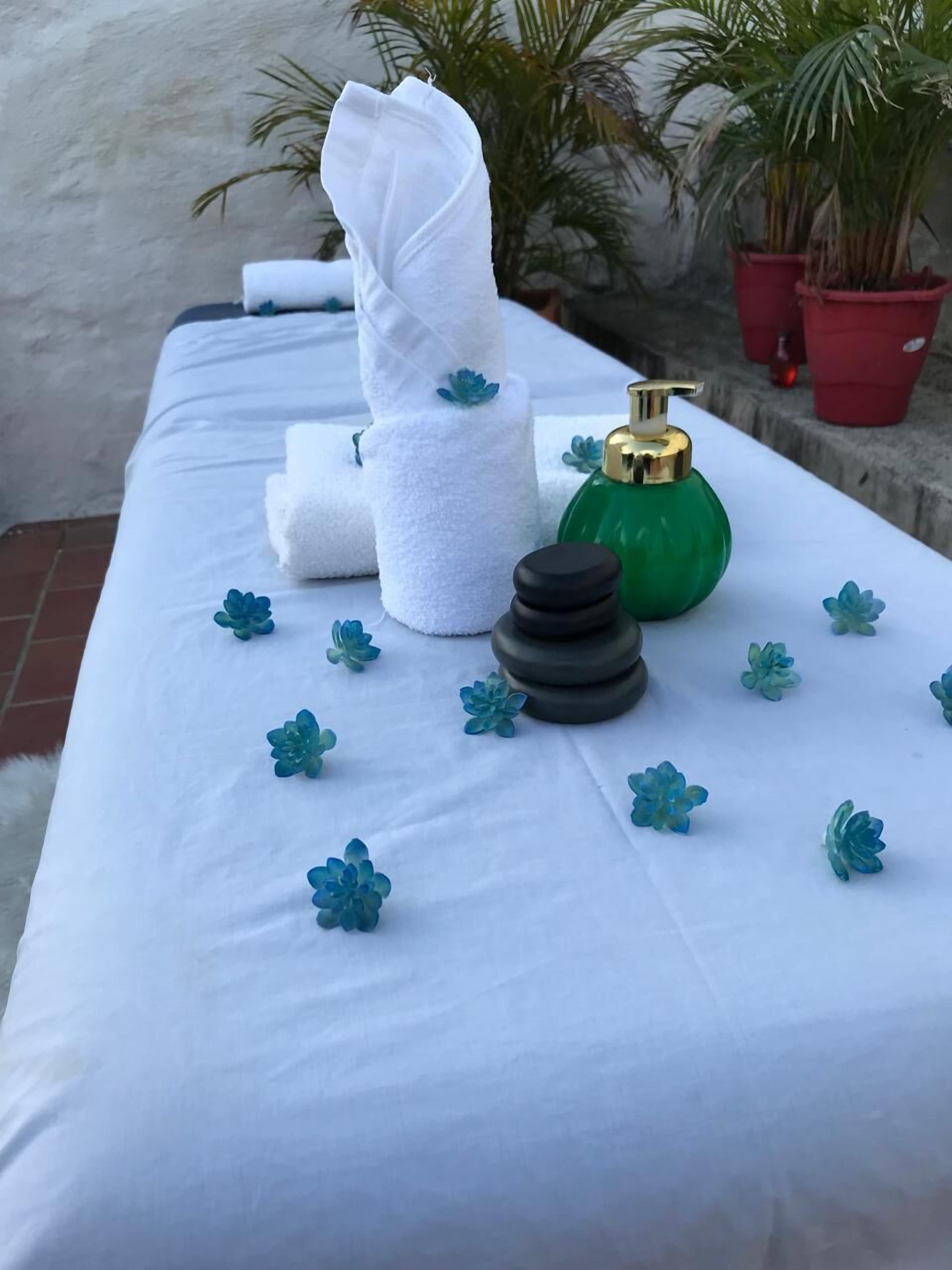 A spa area with a massage table, towels, a massage stone, a green bottle, and decorative flowers.