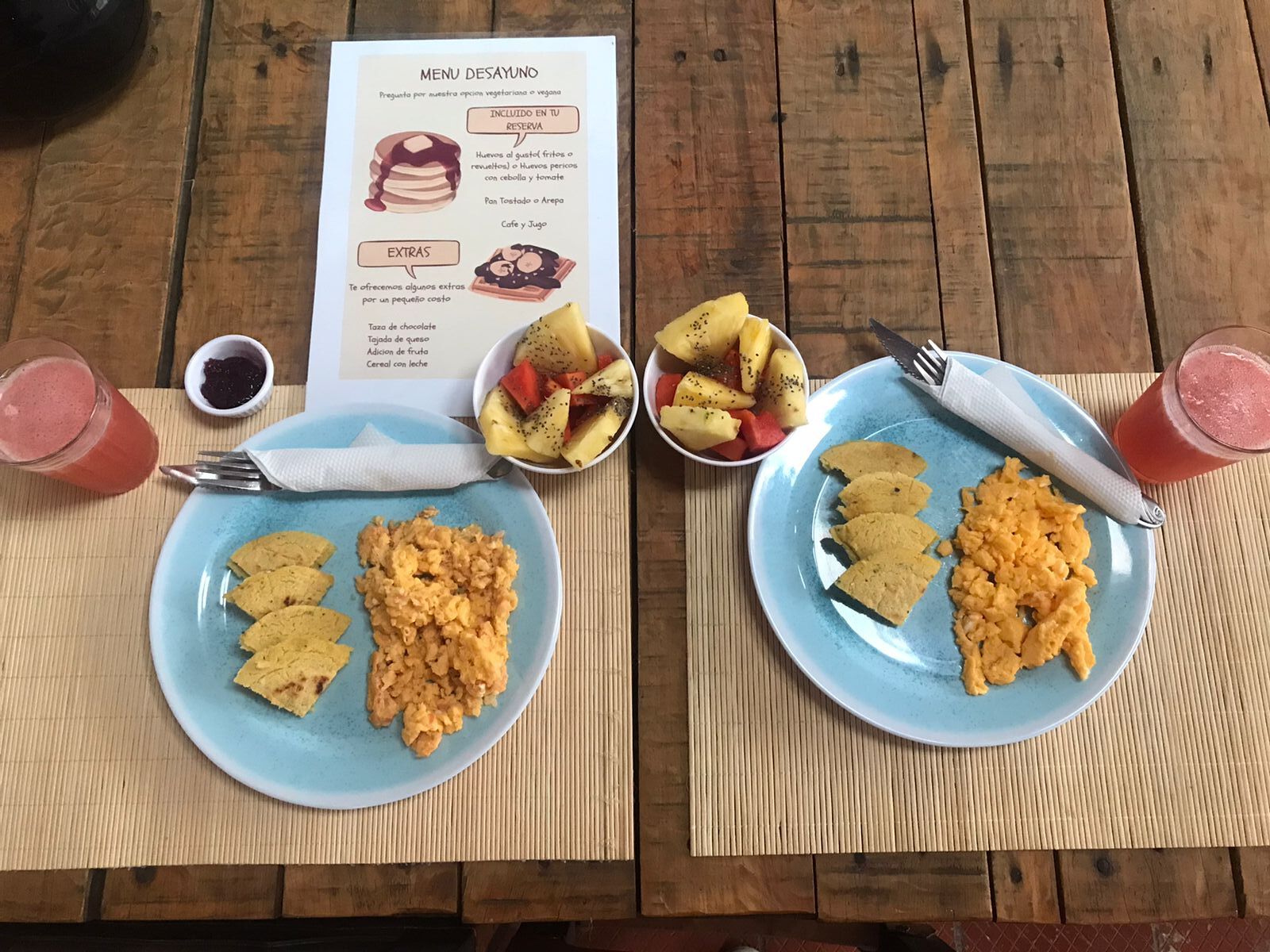 A wooden table with two plates of food, a menu, and a glass of drink.