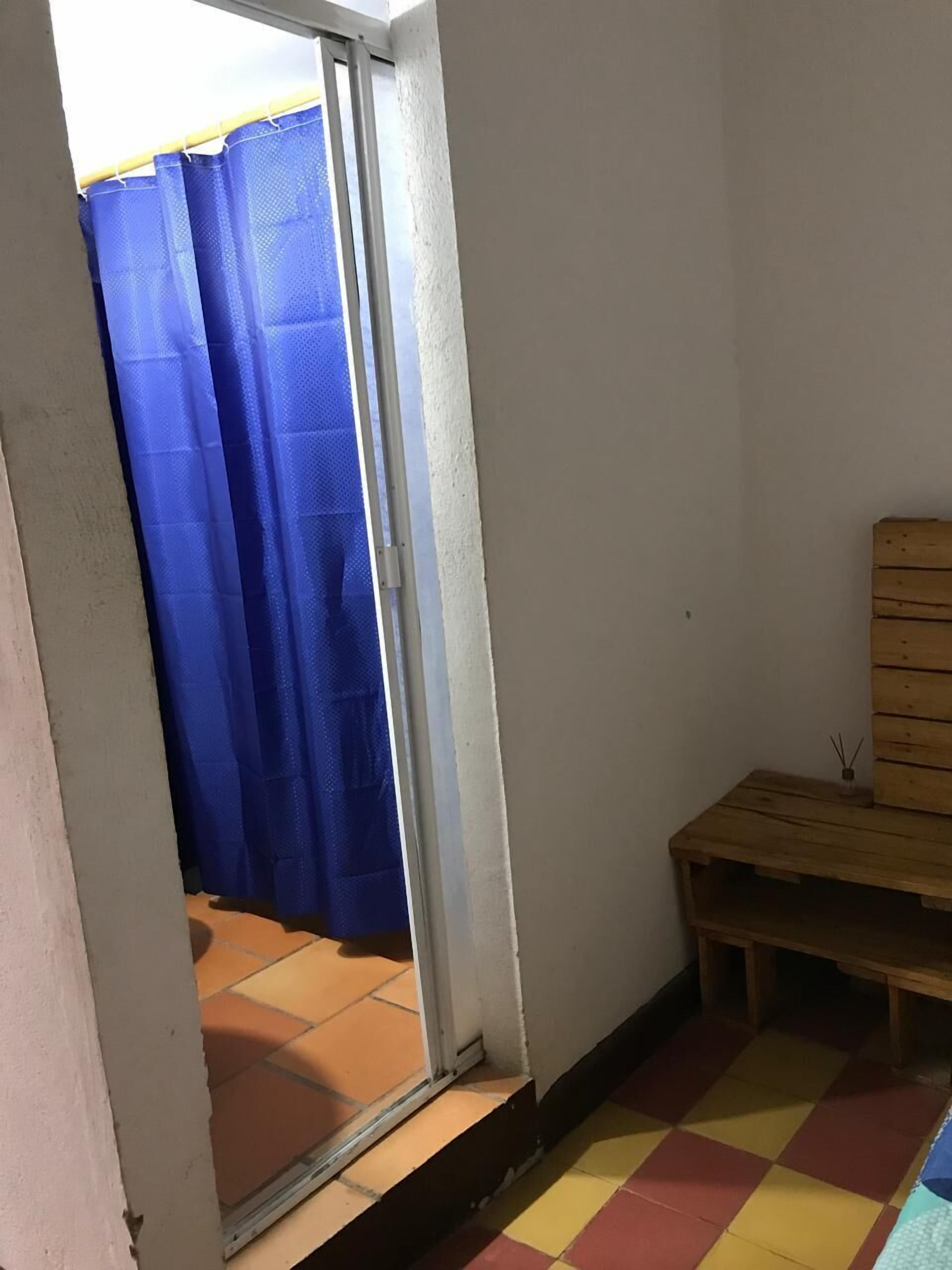 A small room with a wooden bench, a blue curtain, and a tiled floor.