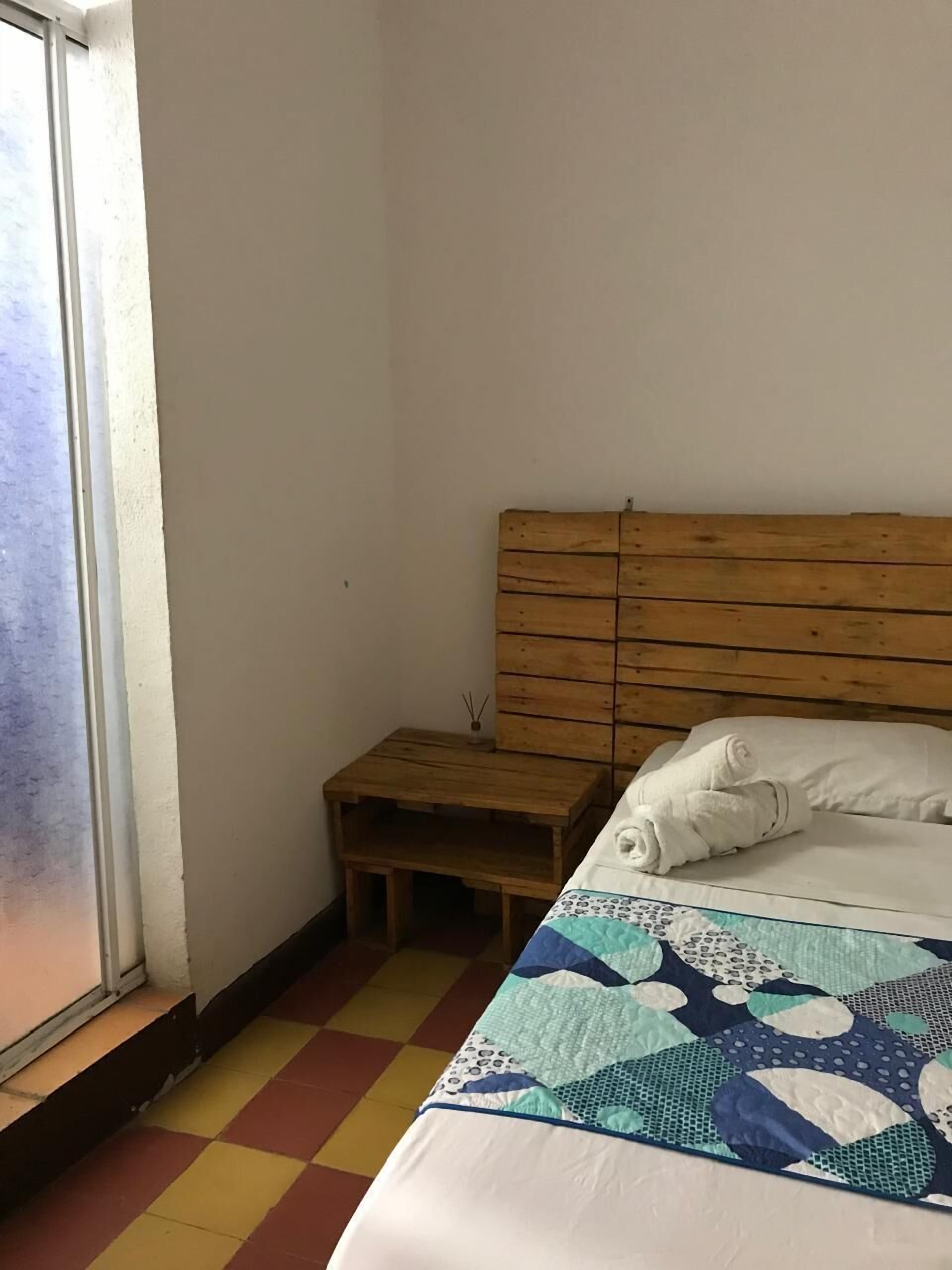 A bedroom with a wooden headboard, a small wooden nightstand, a bed with a patterned quilt, and a window with a view.