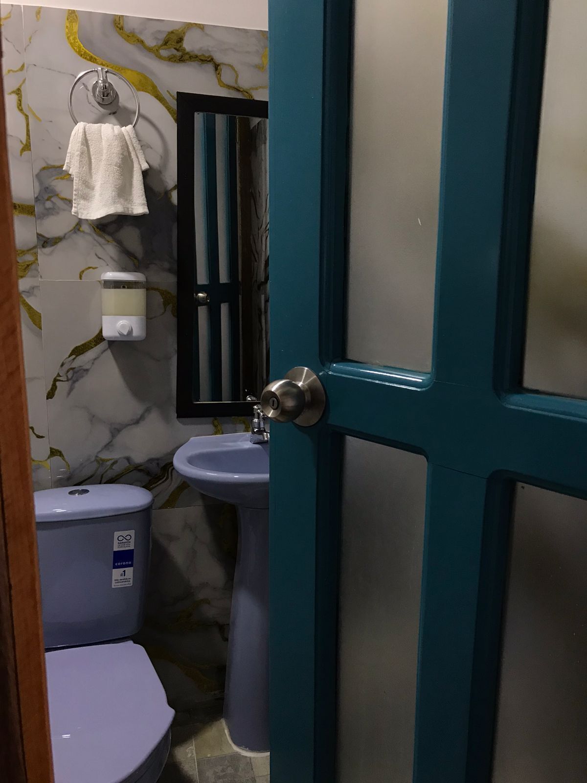A bathroom with a toilet, bidet, and sink. There is a towel hanging on a metal ring, a soap dispenser, and a toilet paper holder.