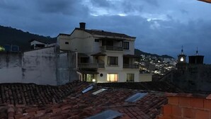 A rooftop terrace with a wooden table and chairs, a tiled roof, and a view of a cityscape at dusk. - The Best Adventure (San Gil)