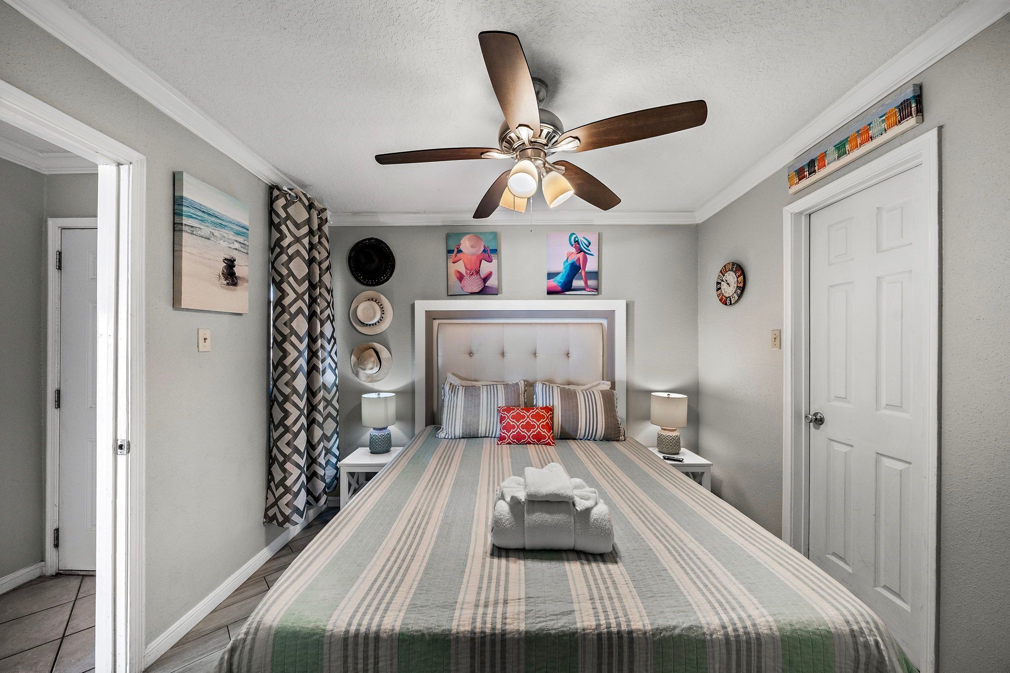 A bedroom with a bed, a ceiling fan, a bedside table, a nightstand, and a wall clock.