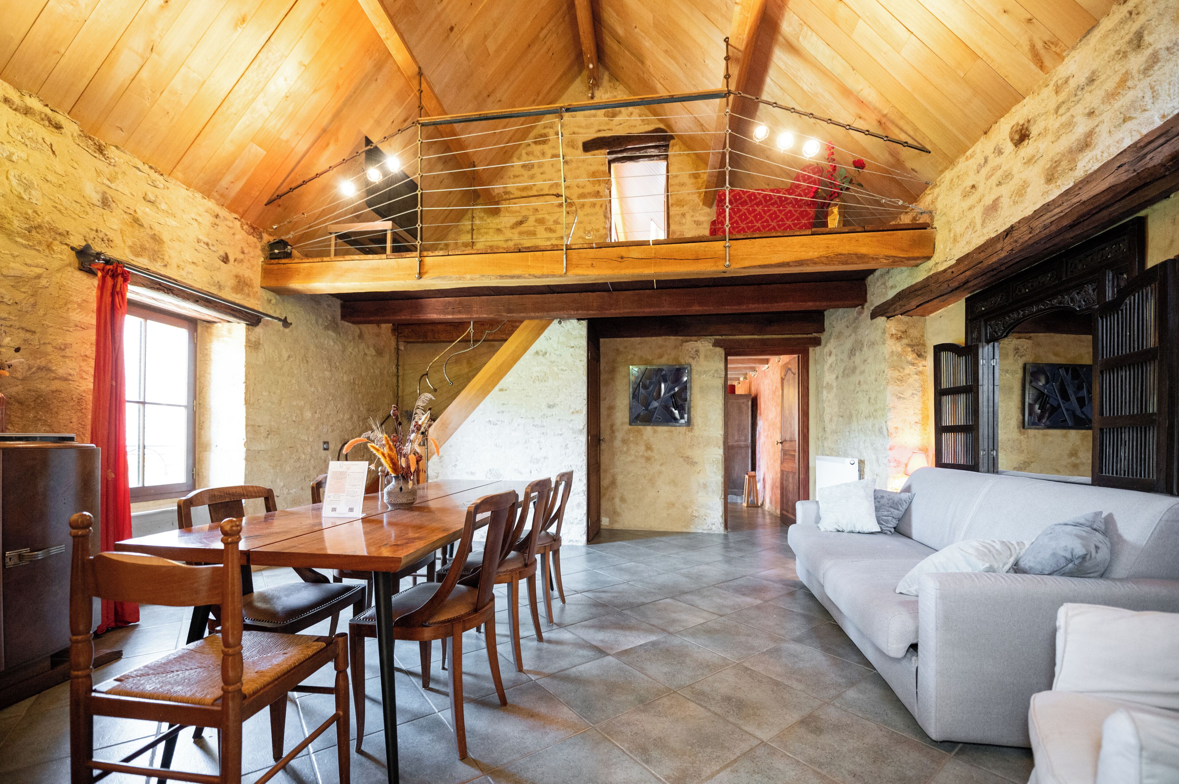 A dining area with a wooden table and chairs, a white sofa, and a loft space with a railing.