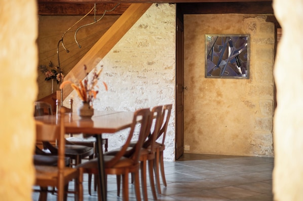 A dining area with a wooden table and chairs, a stone wall, and a window with a metal frame.