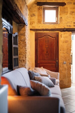 A cozy room with a stone wall, a wooden door, and a cushioned seating area. - The Gîte (VITRAC)