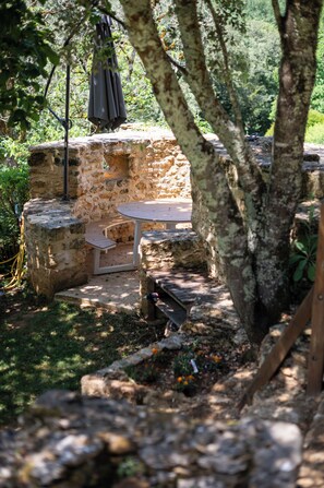 Uma área de estar ao ar livre rústica, com paredes de pedra, uma mesa de madeira e um banco.