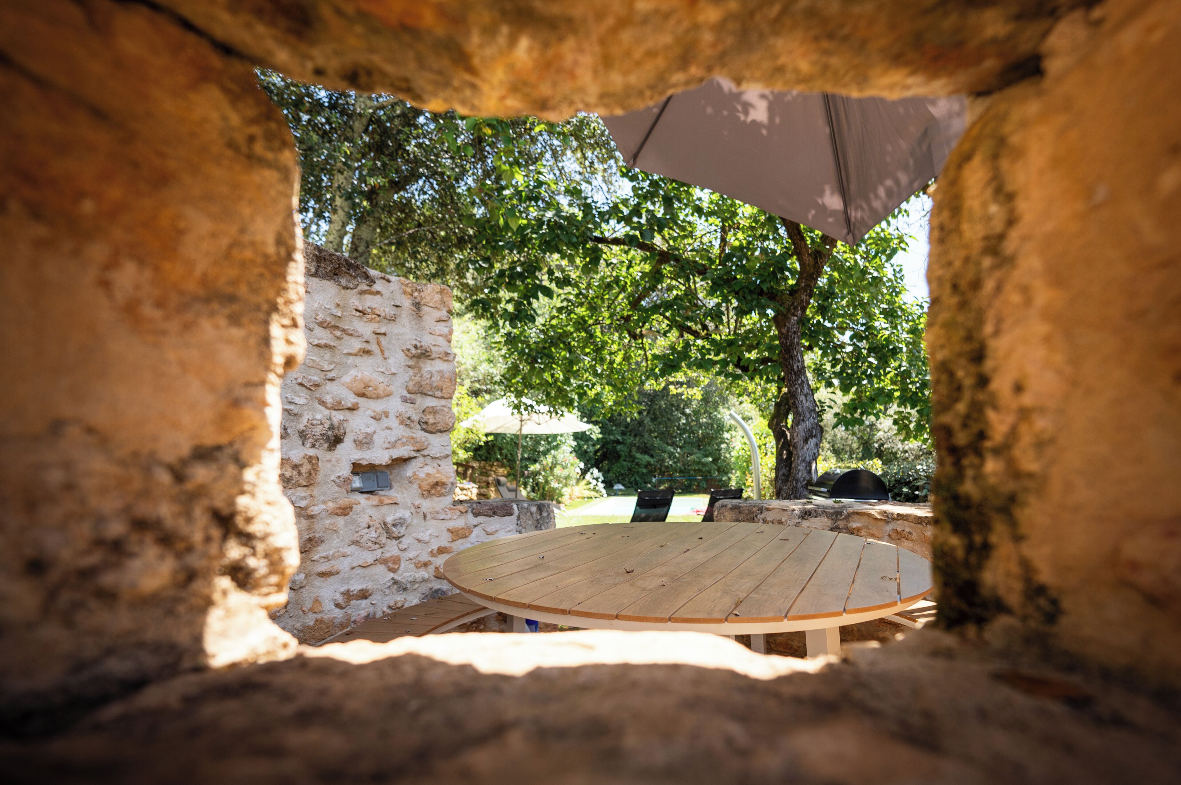 A stone wall with a wooden table and chairs under a canopy.