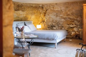 A bedroom with a stone wall, a bed, a bedside table, and a lamp. - The Troglodyte cave Suite (VITRAC)