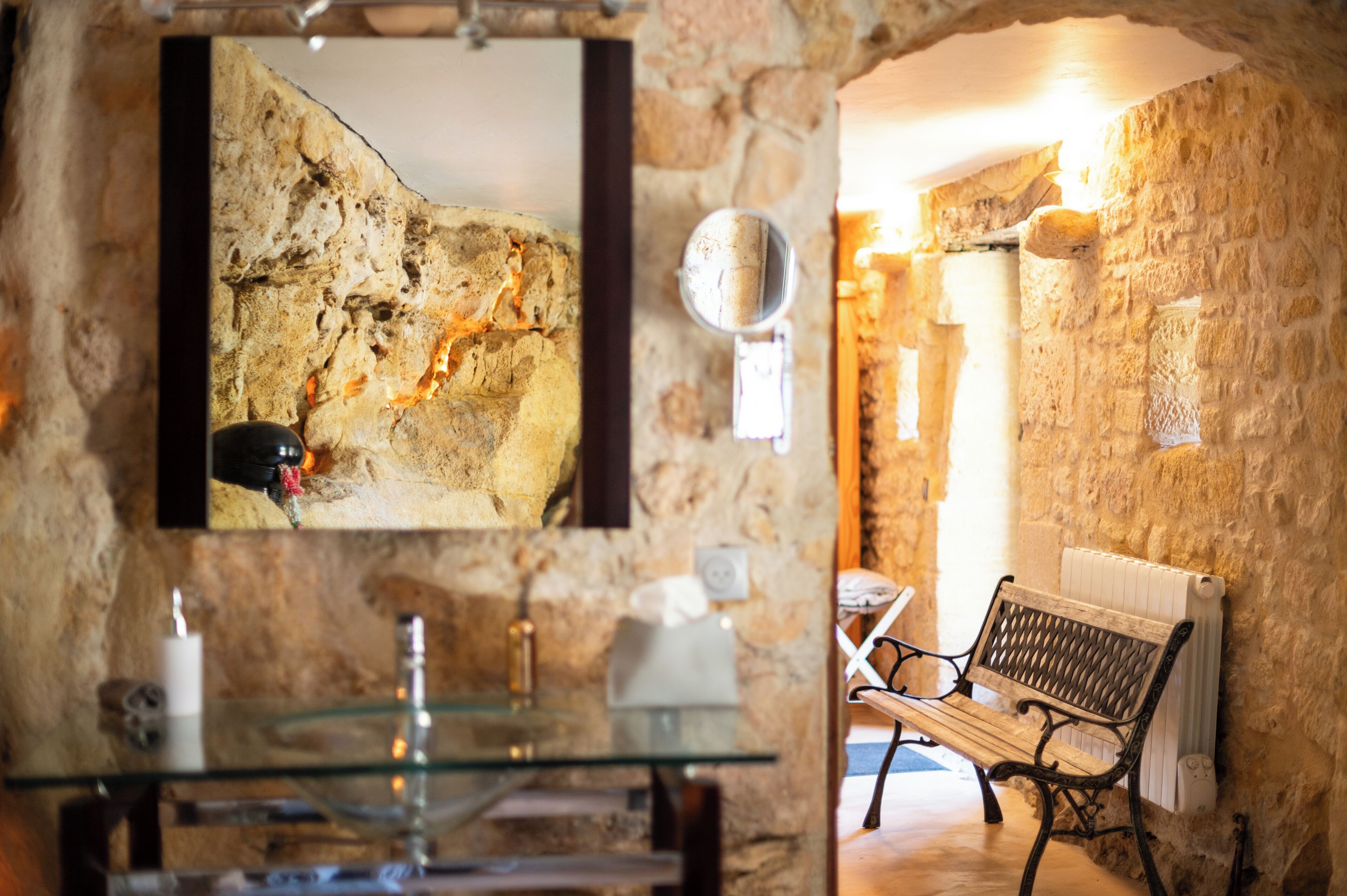 A stone-walled room with a glass table, a bench, and a framed picture on the wall.