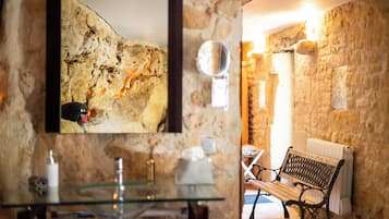 A stone-walled room with a glass table, a bench, and a framed picture on the wall.