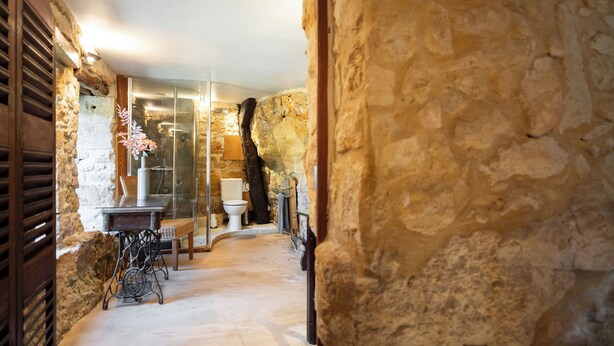 A stone-walled bathroom with a shower, a toilet, and a sink. - The Troglodyte cave Suite (VITRAC)