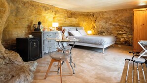 A bedroom with a stone wall, a bed, a desk with a lamp, and a chair. - The Troglodyte cave Suite (VITRAC)