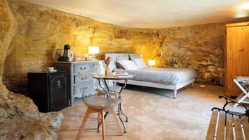 Une chambre avec un mur en pierre, un lit, un bureau avec une lampe et une chaise.