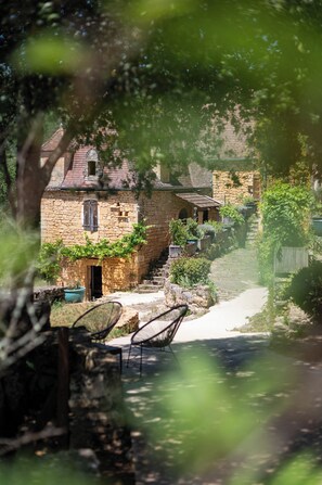 A stone building with a sloped roof, a small door, and a window. There are steps leading up to the entrance, and a pathway beside the building. - The Troglodyte cave Suite (VITRAC)