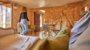 A rustic room with stone walls, a bed, a table with chairs, and a window with shutters. - The Troglodyte cave Suite (VITRAC)