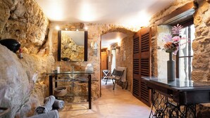 A stone-walled bathroom with a glass sink, a bench, and a mirror. - The Troglodyte cave Suite (VITRAC)