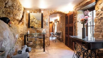 Une salle de bain aux murs en pierre, dotée d’un lavabo en verre, d’un banc et d’un miroir.