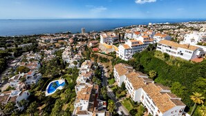 A coastal residential area with white buildings, a swimming pool, and a view of the sea. - Delfin | Pool - terrace - golf (Mijas Costa)