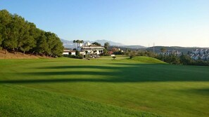 A golf course with a clubhouse, trees, and a distant mountain range.