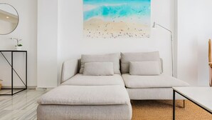 A modern living room with a sofa set, a painting of a beach scene, a round mirror, and a small table with a plant.