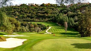 A golf course with sand bunkers, trees, and a hilly backdrop.