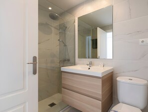 A modern bathroom with a glass shower enclosure, a white sink with a wooden vanity, and a toilet.