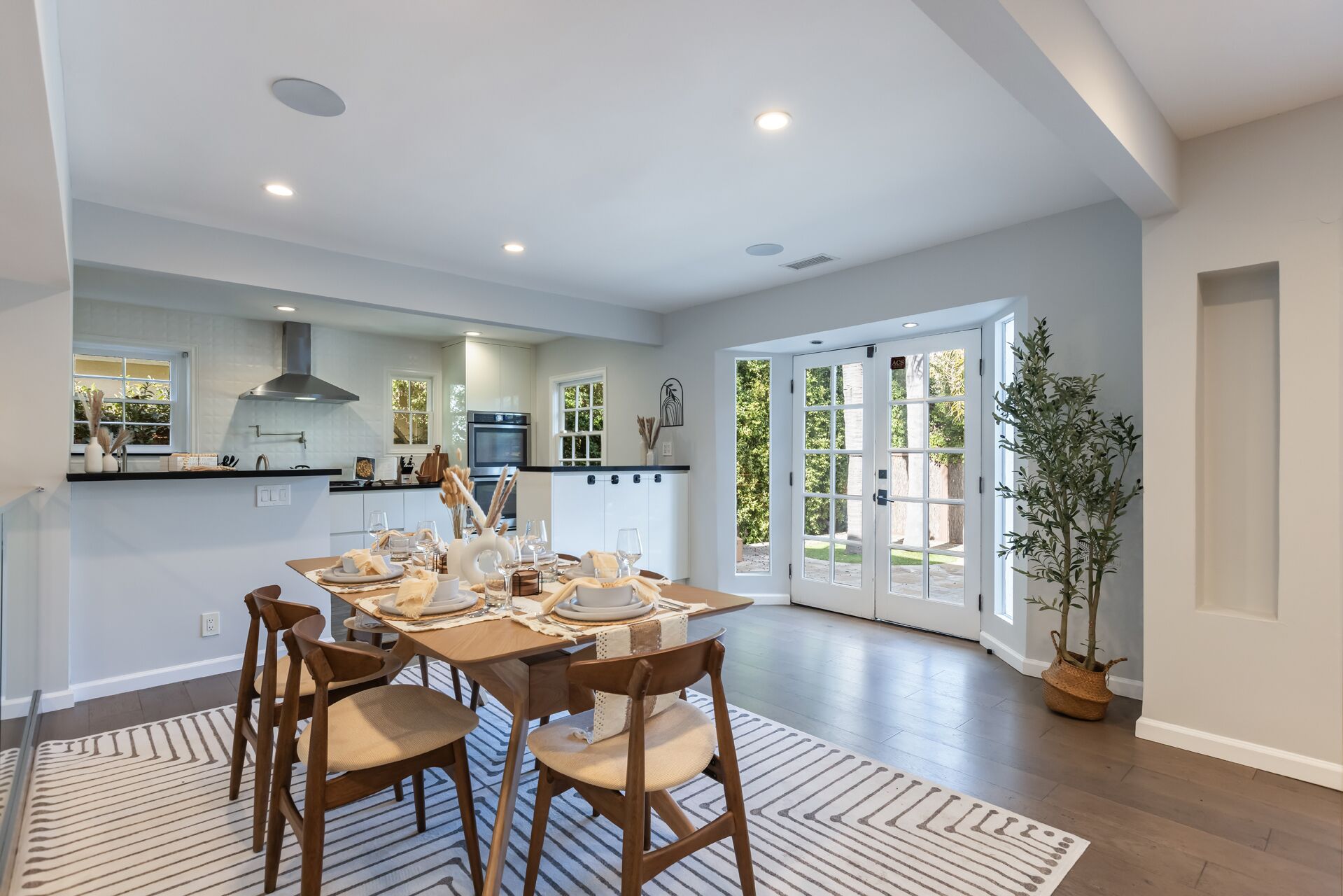 A modern kitchen with white cabinets, a black countertop, and a dining area with a wooden table and chairs.