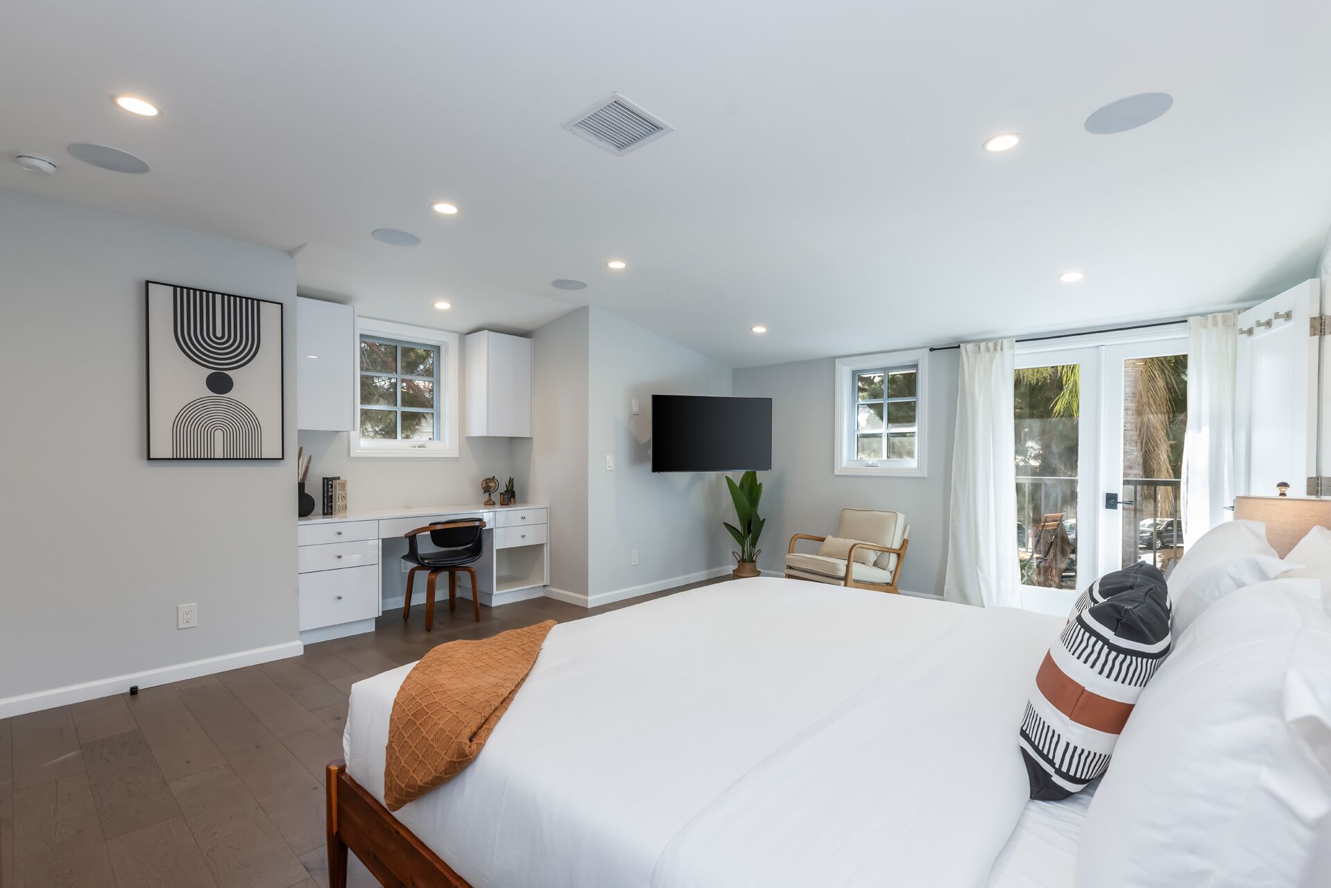 A modern bedroom with a large bed, a desk, and a TV.