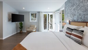 A modern bedroom with a large bed, a flat-screen TV, a chair, and a balcony with glass doors. - Casa Estrella by Oraklus (Los Angeles)