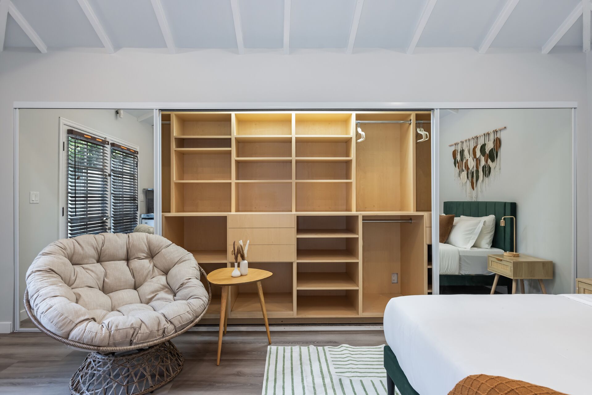 A bedroom with a large walk-in closet, a comfortable chair, a bedside table, and a bed.