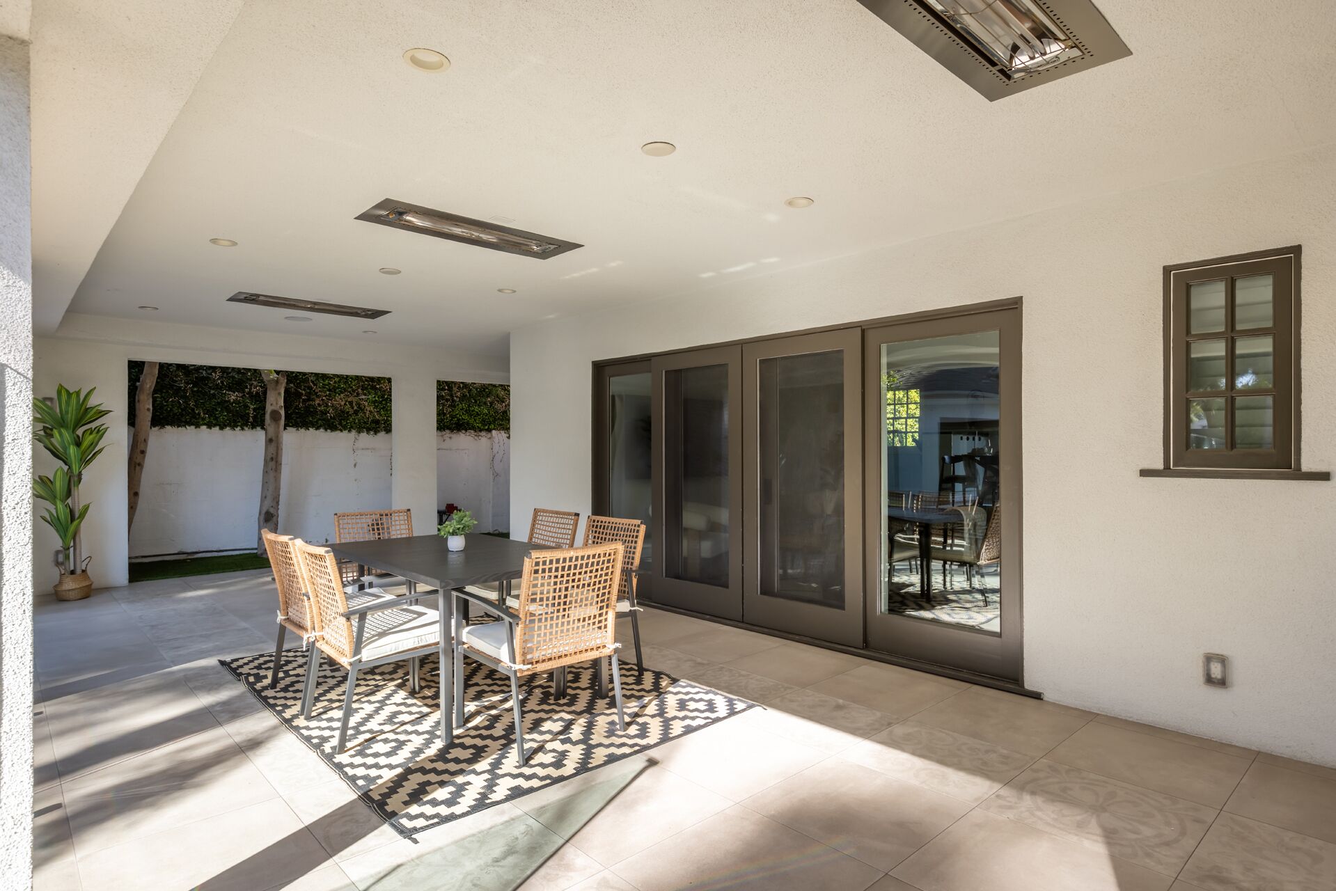 A dining area with a table and chairs, a patterned rug, and a view through a glass door.