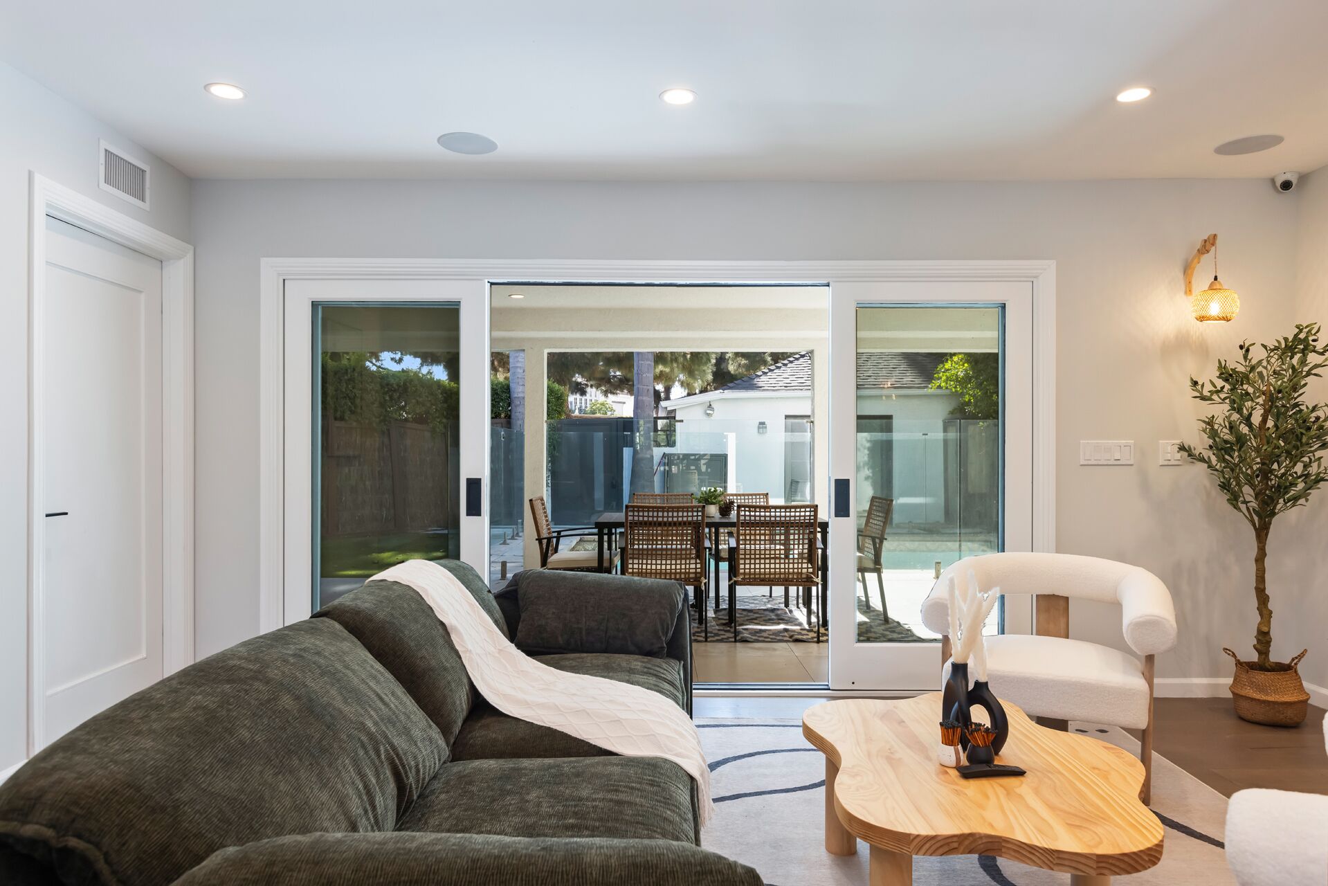 A modern living room with a sofa, a coffee table, and a chair. There is a sliding glass door leading to an outdoor patio with a table and chairs.