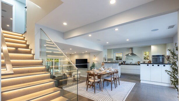A modern kitchen with white cabinets, a central island, and a dining area with a glass railing. - Casa Estrella by Oraklus (Los Angeles)
