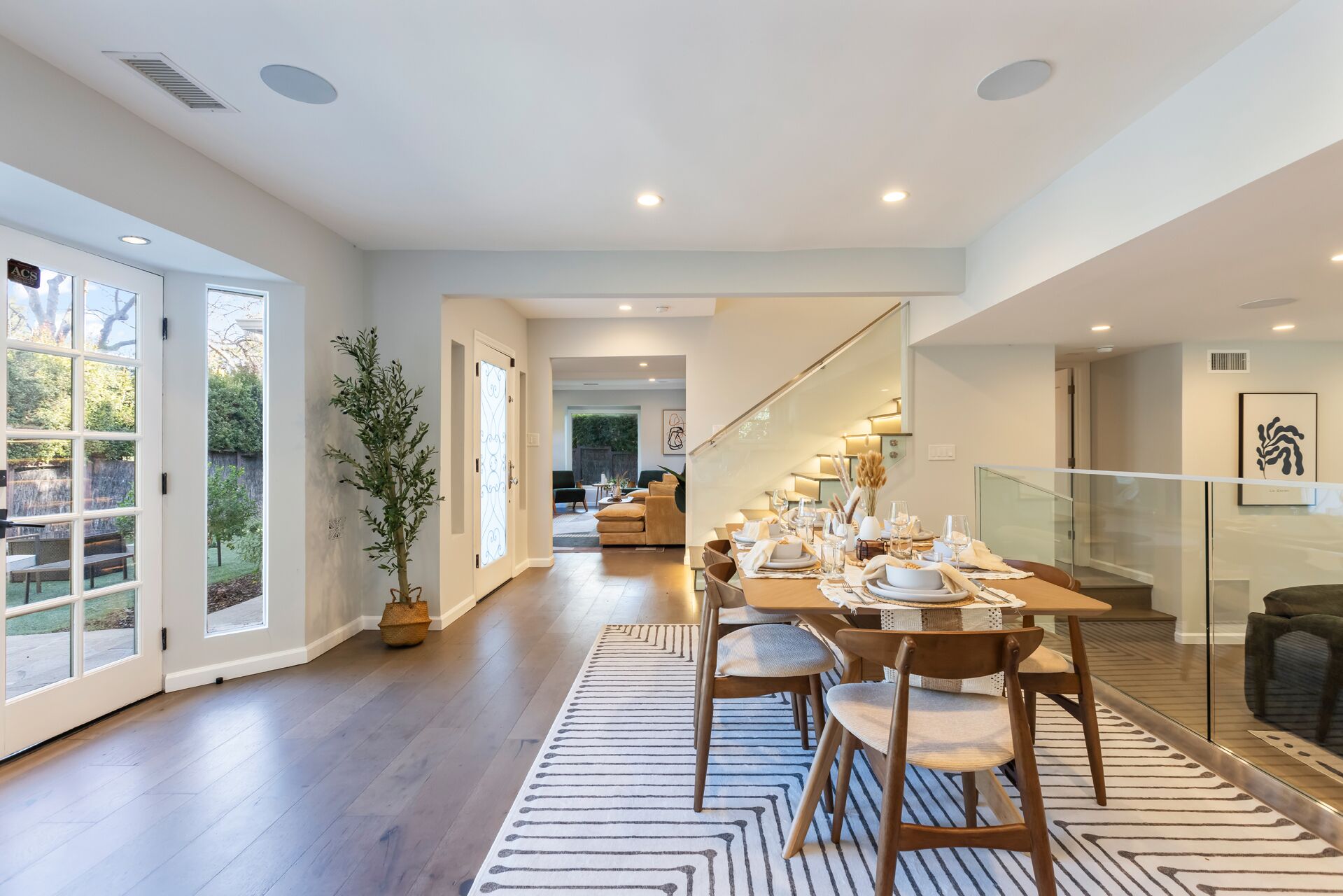 A spacious dining area with a long table set for six, a potted plant, and a view of the backyard through large sliding doors.