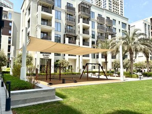 A residential building with multiple balconies, a shaded outdoor area with a swing set, and a sign for 'SUNSET'. - Stylish 1 BD Getaway in Dubai Creek Beach (Dubai)