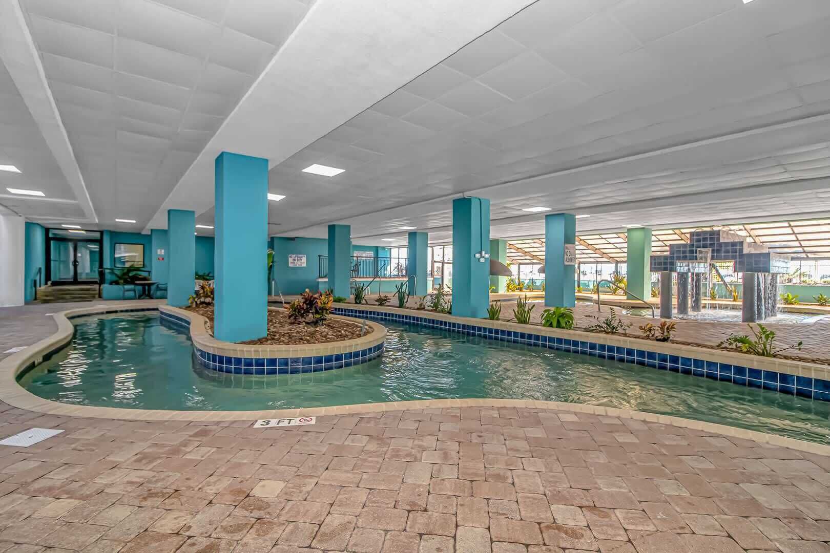 Una piscina interior con borde de azulejos, rodeada de suelo de ladrillo y sostenida por pilares azules.
