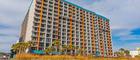 A multi-story hotel with a modern architectural design, featuring balconies and a beach view.