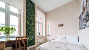 Un dormitorio con cama, escritorio, silla, ventana y una pared con un diseño de hojas verdes.