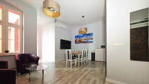 Una sala moderna con comedor, un ventanal con contraventanas rojas, un televisor de pantalla plana y un cuadro en la pared.