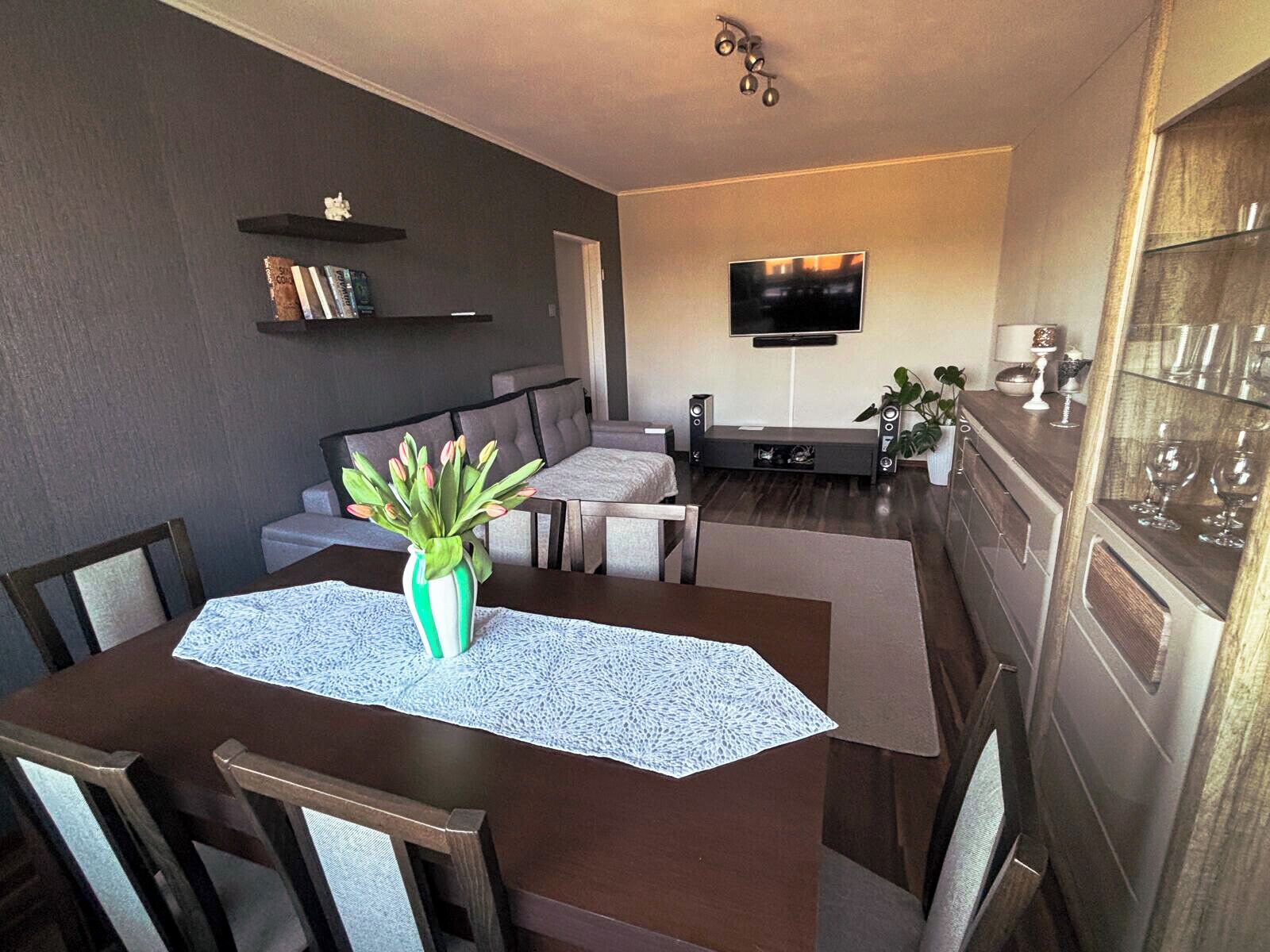 Ein Essbereich mit einem Tisch, der für vier Personen gedeckt ist, einer Blumenvase und einem Fernseher im Hintergrund.