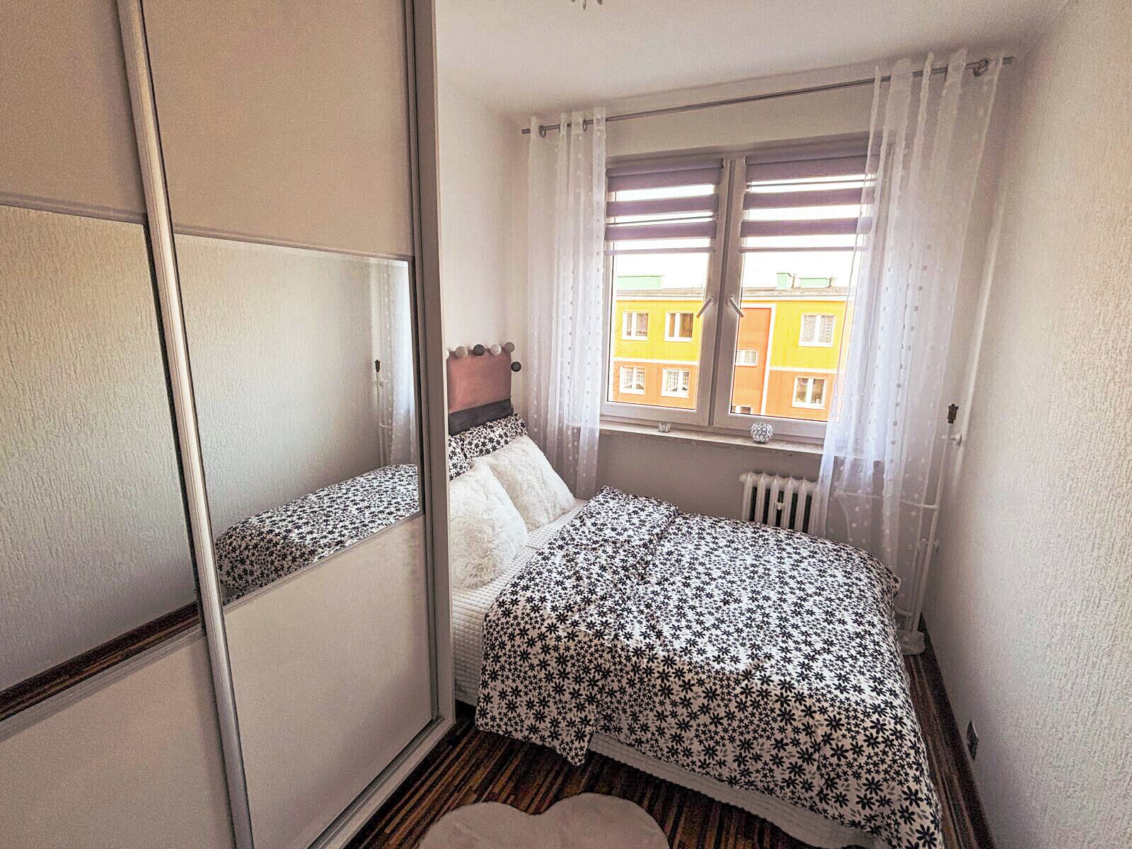 Une petite pièce, de taille modeste, comprenant un lit, une fenêtre avec des rideaux et un radiateur.