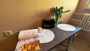 Ruokapöydällä on kirja, leivänpaahdin ja maljakko, jossa on kukkia.