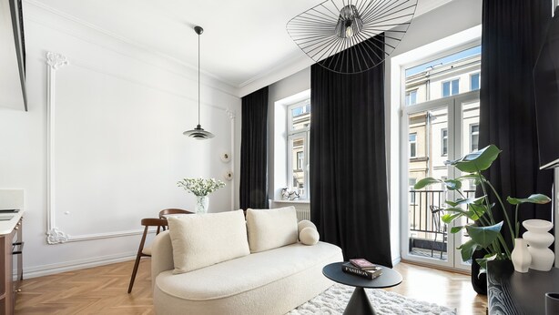 A modern living room with a sofa, a coffee table, a potted plant, and a view of the city through large windows.