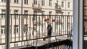 A balcony with a patterned floor, a table with chairs, and a vase with flowers.