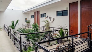 Un edificio moderno con un espacio exterior cubierto, que incluye una escalera, plantas en macetas y un tragaluz.